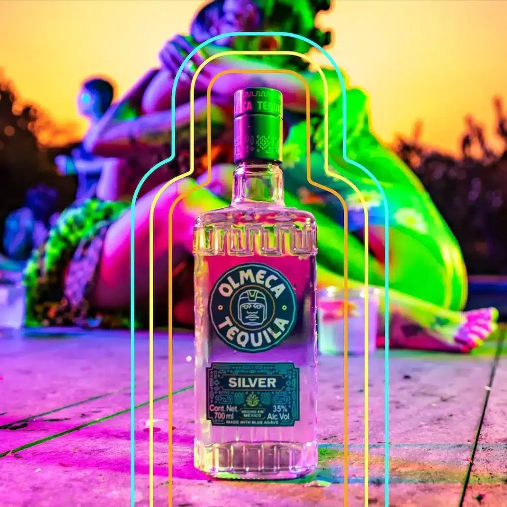 bottle of olmeca silver tequila in the background two friends hugging in a valentines party decorations